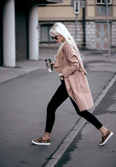 Beautiful blonde model walking outdoors with coffee