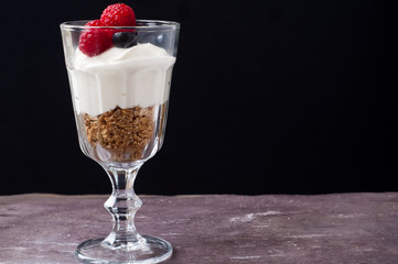 A glass of healthy breakfast muesli with yogurt and topped with fresh raspberries and blueberries.