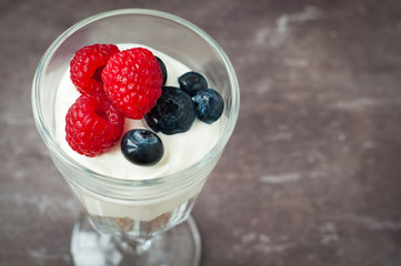A glass of healthy breakfast muesli with yogurt and topped with fresh raspberries and blueberries.