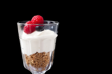A glass of healthy breakfast muesli with yogurt and topped with fresh raspberries and blueberries.