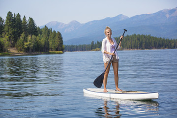 Beautiful woman paddleboarding on scenic mountain lake 