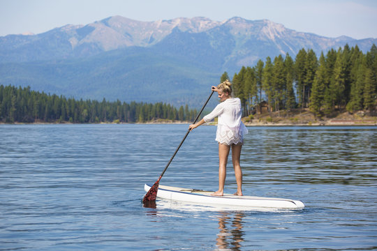 Beautiful woman paddleboarding on scenic mountain lake 