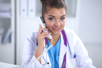 Beautiful young smiling female doctor sitting at the desk and writing.