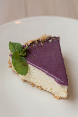 Cheesecake with purple icing lying on a plate, decorated with leaves of fresh mint