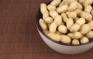 peanuts on a brown background in a ceramic bowl