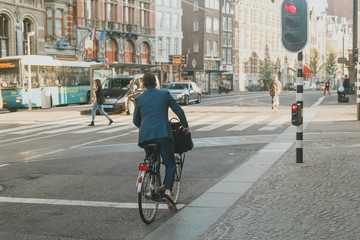 a man in a suit on a bicycle in the city stands until glowing red light. He goes to wor