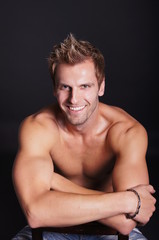 Fototapeta premium Smiling young man sitting on dark background