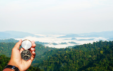 Man hand with a black and silver compass in green mountain blur.