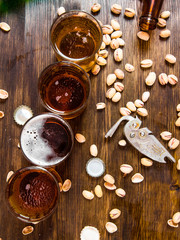 Four beers with pistachios on a wooden table.