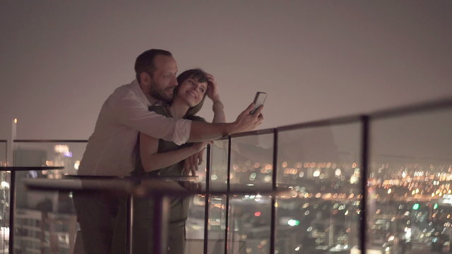 Young couple taking selfie photo on rooftop terrace at night