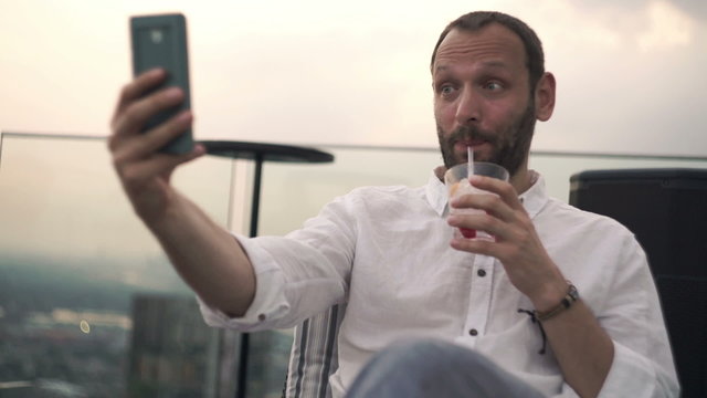 Happy man with cocktail taking selfie photo with cellphone in bar
