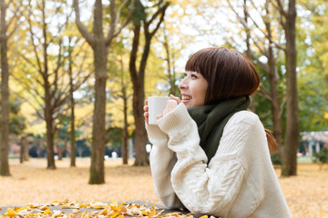 紅葉した森でコーヒーを飲む女性