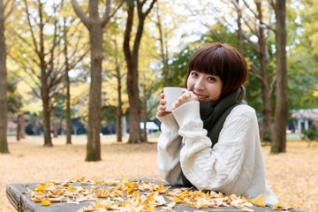 紅葉した森でコーヒーを飲む女性