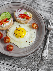 Fried eggs, tomatoes and sandwiches with cucumber, radish and soft cheese. On a light wooden table. Rustic style. Healthy breakfast or snack