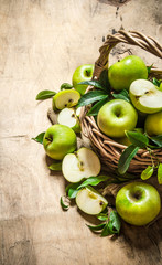 Green apples in an old basket. On wooden table.