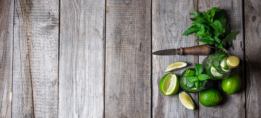 Cocktail in glass and bottle , also mint and limes on a wooden table . Free space for text.