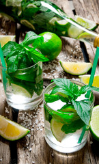 Freshly made mojito in glass and the bottle with mint and lime, sugar and rum. On a wooden table.