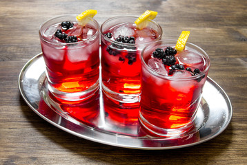 Berry cocktails in glass with ice and lemon on wooden table .