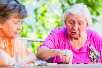 Two senior ladies playing board game in rest home