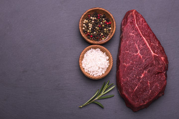 Raw Beef Steak, salt, pepper, garlic, rosemary  on the black board, background.