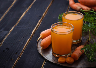 Glasses of carrot juice on black background