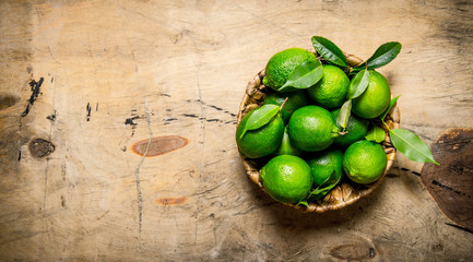 Fresh limes in a Cup with leaves. On wooden table.