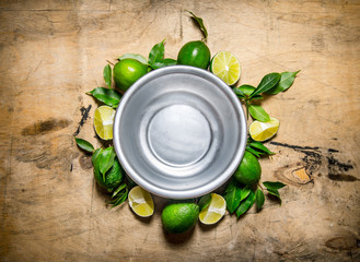 Fototapeta na wymiar Empty bowl with slices of fresh limes and leaves around.