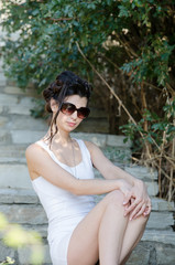 Sexy slim lady wear tight short white dress and sunglasses, sitting on stairs with her legs crossed on the side