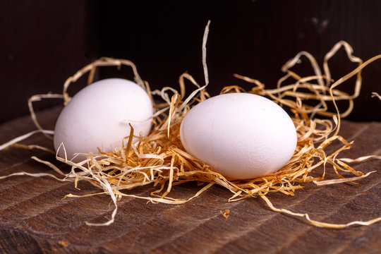 Two white chicken eggs lying on the dark Board on the dry grass.