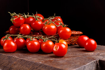 Branch of red tomatoes lying in a basket on a dark table.