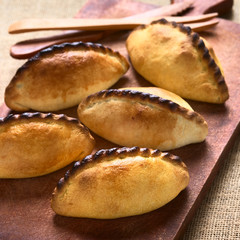Traditional Bolivian savory pastries called Saltena filled with thick meat stew, photographed with natural light (Selective Focus, Focus on the first saltena)