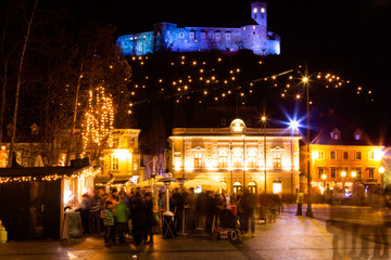 Fototapeta na wymiar Ljubljana, Slovenia - November 27, 2015. People drink mulled wine on Congress square near festive loge on the background of illuminated castle.