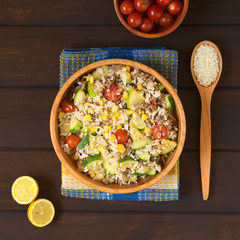Rice dish with mincemeat and vegetables (sweet corn, cherry tomato, zucchini, onion) in wooden bowl with ingredients on the side, photographed on dish towel on dark wood with natural light