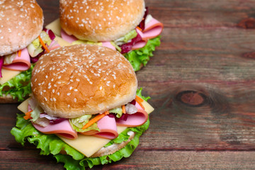 Burger sandwich with sausage, cheese and vegetables on a wooden background