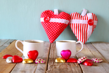 image of two red heart shape chocolates and couple cups of coffee on wooden table. valentine's day celebration concept. vintage filtered
