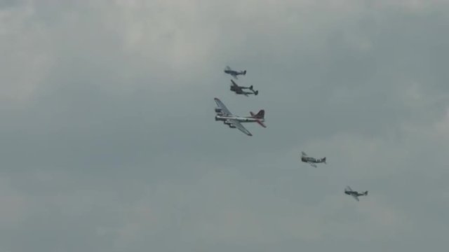 B-17 Flying Fortress leads a formation of four World War II fighter planes, banking in formation, including a P-63 Kingcobra, a P-38 Lightning, and two P-51 Mustangs.