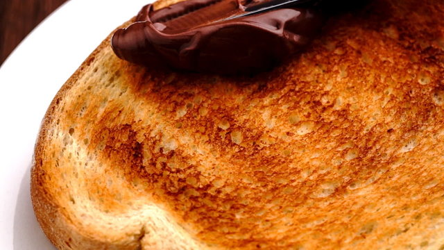 Spreading smooth and sweet hazelnut chocolate spread on freshly toasted bread