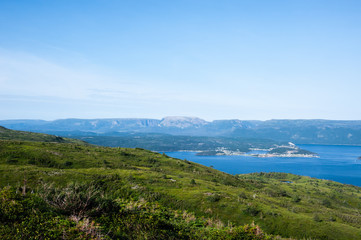Green hills near water against plateau under pale blue sky