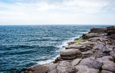 Horizon and rocky coastline with waves splashing under cloudy sk