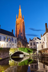 Fototapeta premium little dock and bridge in a canal of Bruges, with Onze-Lieve-Vrouwekerk (Church of Our Lady) as background, Belgium