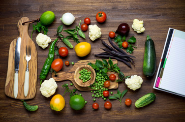 Healthy food. Herbs and vegetables on wooden table with recipe book. Top view. 