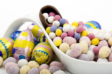 Fototapeta premium A selection of Easter Eggs in and around a porcelain ladle, with mini eggs spilling out of a larger chocolate egg.