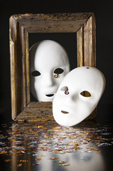 Two white masks, sequins and old frame on a black background