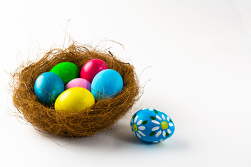 Fototapeta na wymiar Multicolored Easter eggs in a nest and blue Easter egg with floral design on white background. Easter background. Easter symbol. Copy space