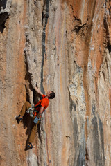 Young man climbs on a rocky wall in a valley with mountains at sunrise.