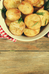 Delicious baked potato with rosemary in bowl on table close up