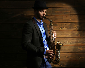 Elegant saxophonist plays jazz on wooden background