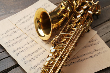Obraz premium Beautiful golden saxophone with musical notes on wooden background, close up