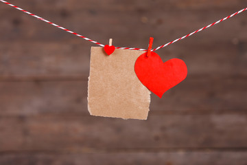 Paper hearts and empty sheet hanging on cord against wooden background