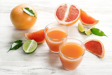 Two glasses of citrus juice and fresh fruits on light wooden background